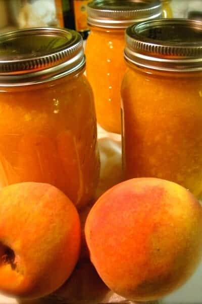 3 jars of canned peach preserves with fresh peaches in front