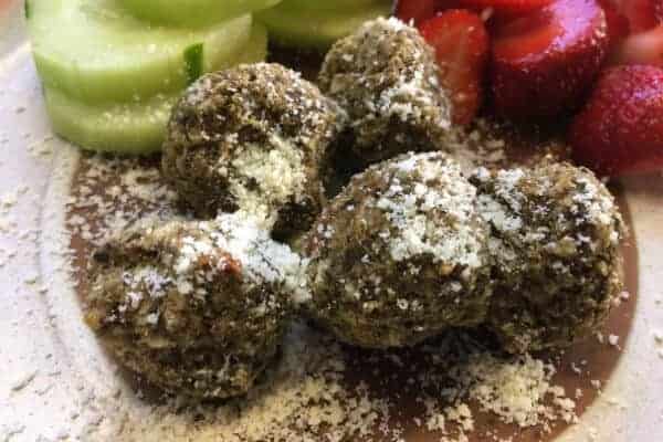 eggplant meatballs sprinkled with parmsean cheese on a plate with cucumbers and strawberries