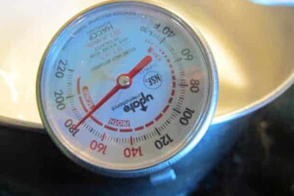 thermometer clipped to the side of a pot of fresh goat milk