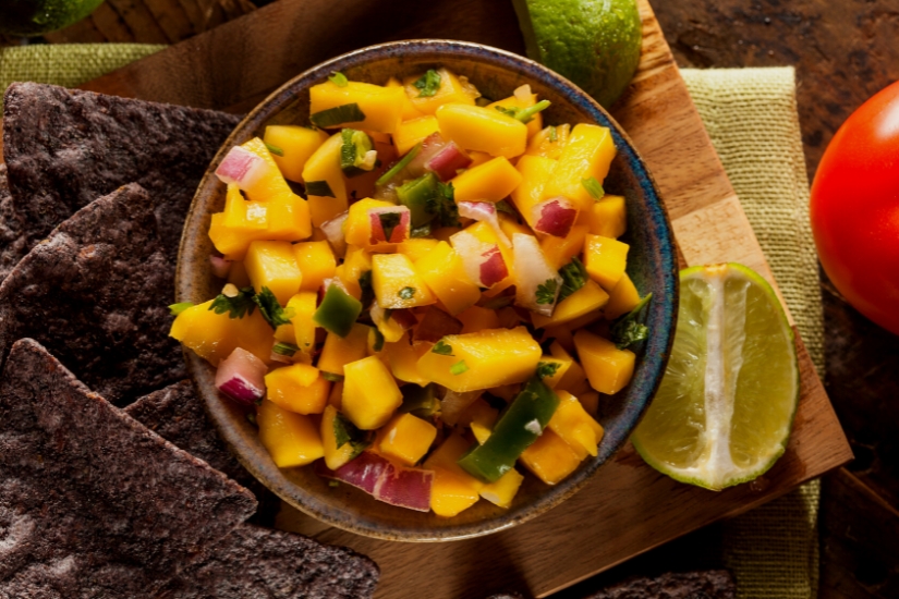 mango salsa on table with chips and limes