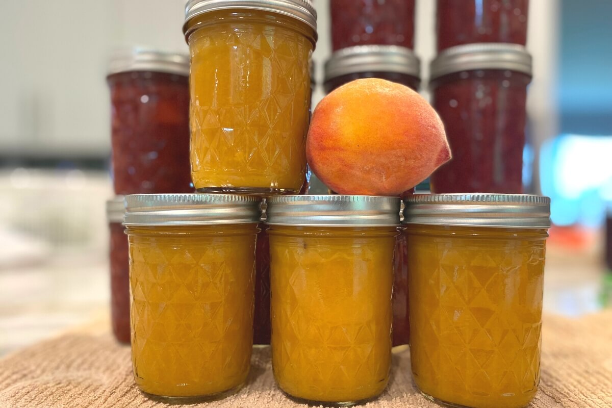 jars of peach preserves with a fresh peach on top of jar