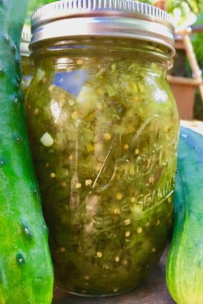close up of homemade pickle relish in a canning jar surrounded by cucumbers